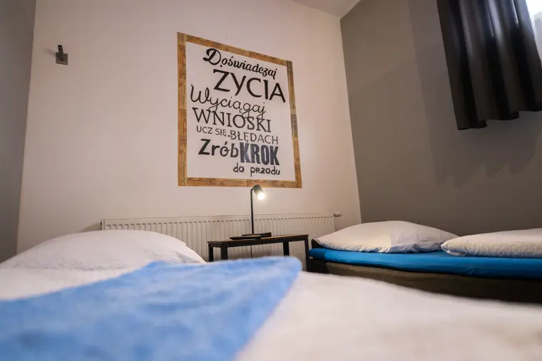 Łóżka z niebieską narzutą i sentencją na ścianie